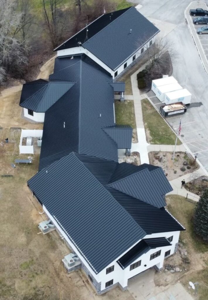 Aerial view of a modern building complex with black metal roofs, white exterior walls, and adjacent parking and walkways—showcasing recent foundation repair work for lasting stability.